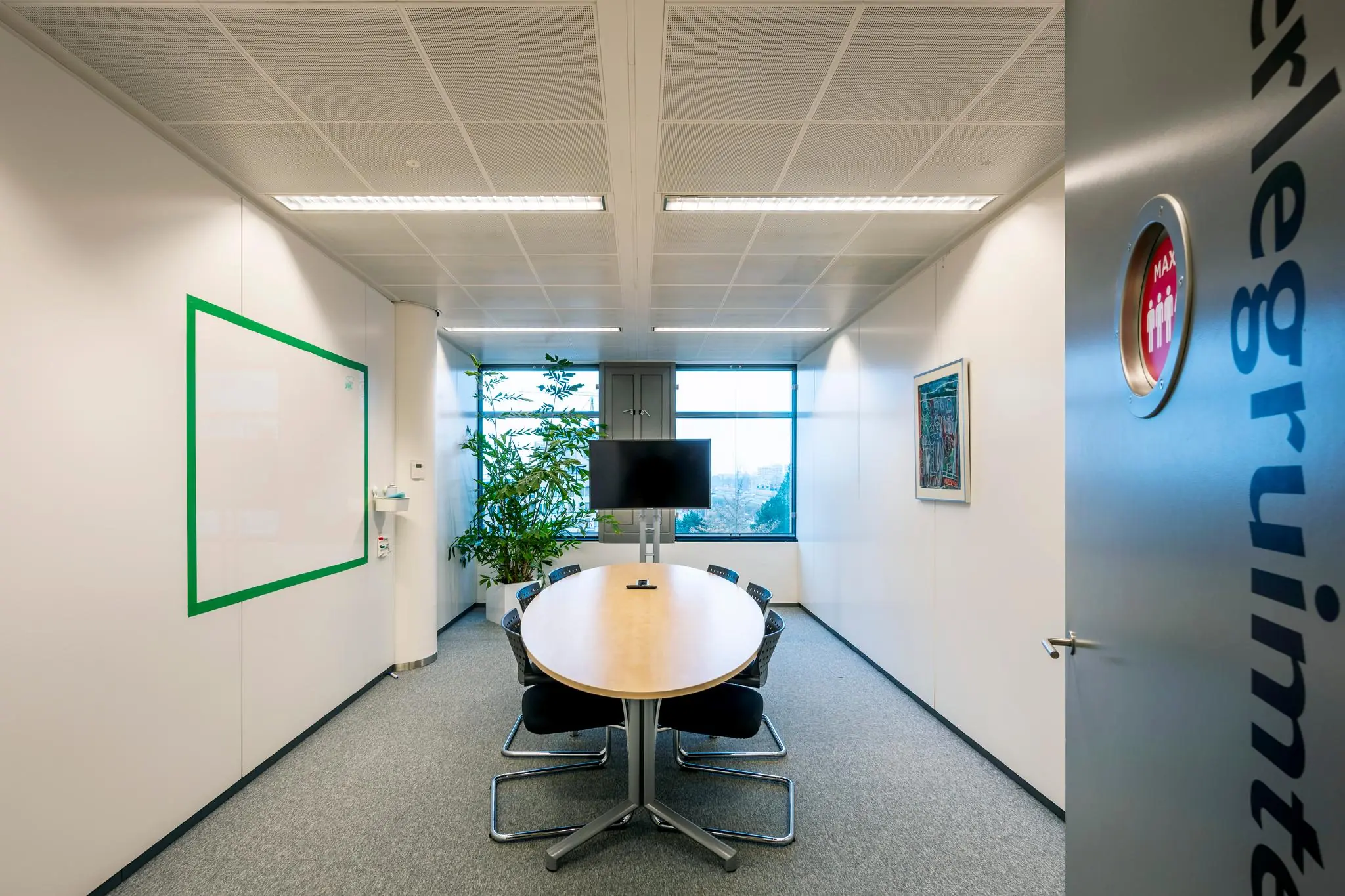 Vergaderruimte aan de Burgemeester Rijnderslaan met ovale tafel, stoelen, tv-scherm en whiteboard.